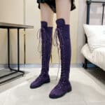 Jambes de femme portant des cuissardes en daim violet, avec des lacets, dans une chambre