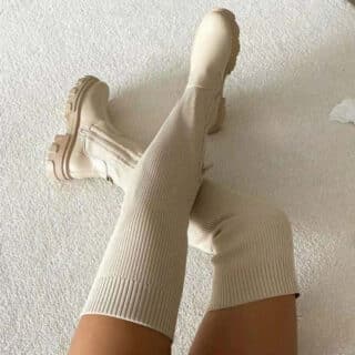 Bottes chaussettes beige portées par une femme. Elles montent au dessus du genou.