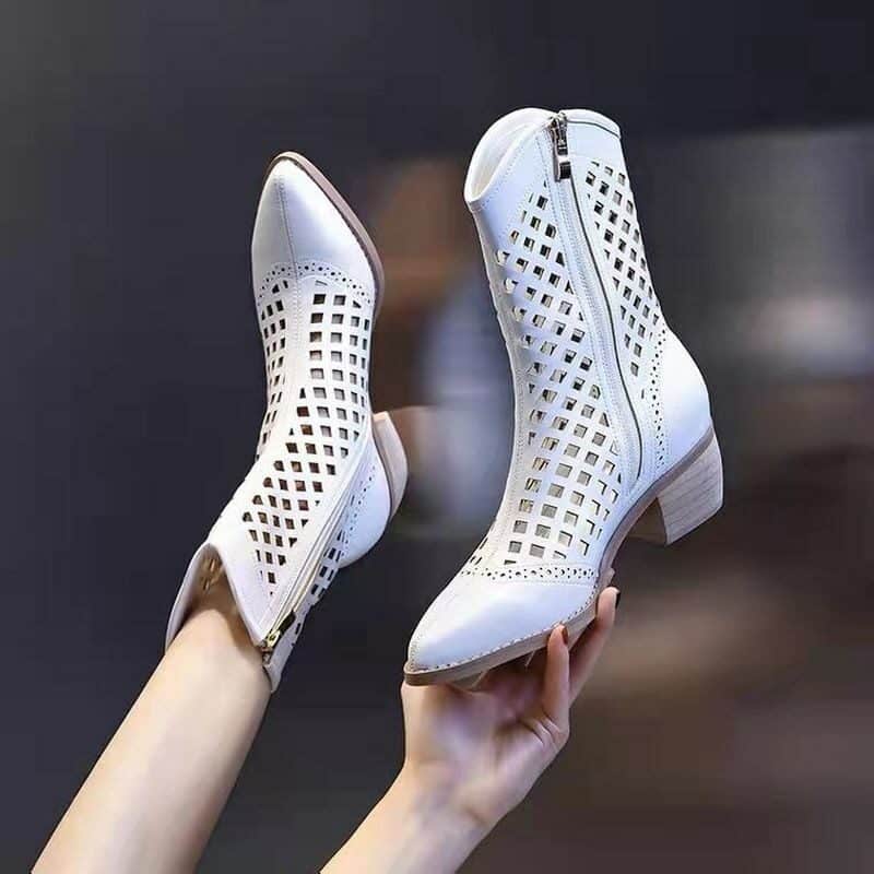 Photo d'une paire de bottes blanche style santiags mi-hautes à bout pointu en cuir PU ajouré. Une botte est porté sur un pied et l'autre est tenue dans une main.