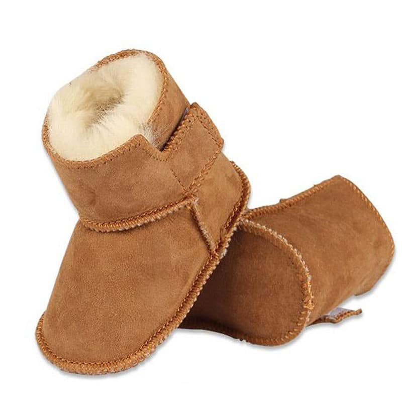 On voit une paire de bottes pour bébé effet cuir retourné camel, à scratch, fourrée en matière polaire blanche, comme du lainage.