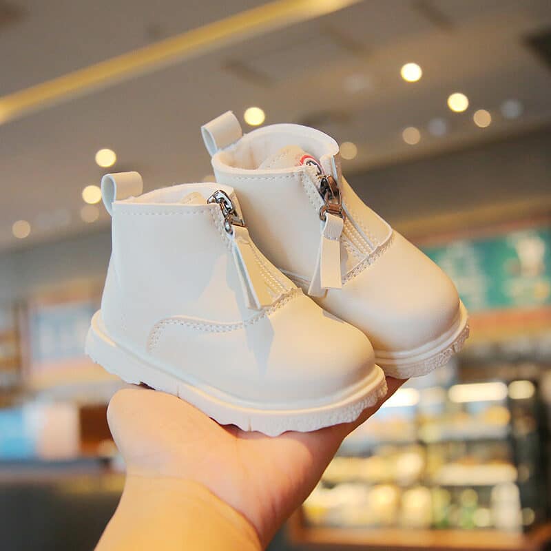On voit une main exposer des bottes courtes crème avec une fermeture zippée à l'avant. La photo est prise dans un magasin de chaussures