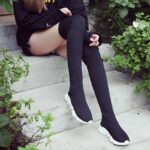 Jambes de femme assise sur des escaliers, verdure, bottes chaussettes baskets noires