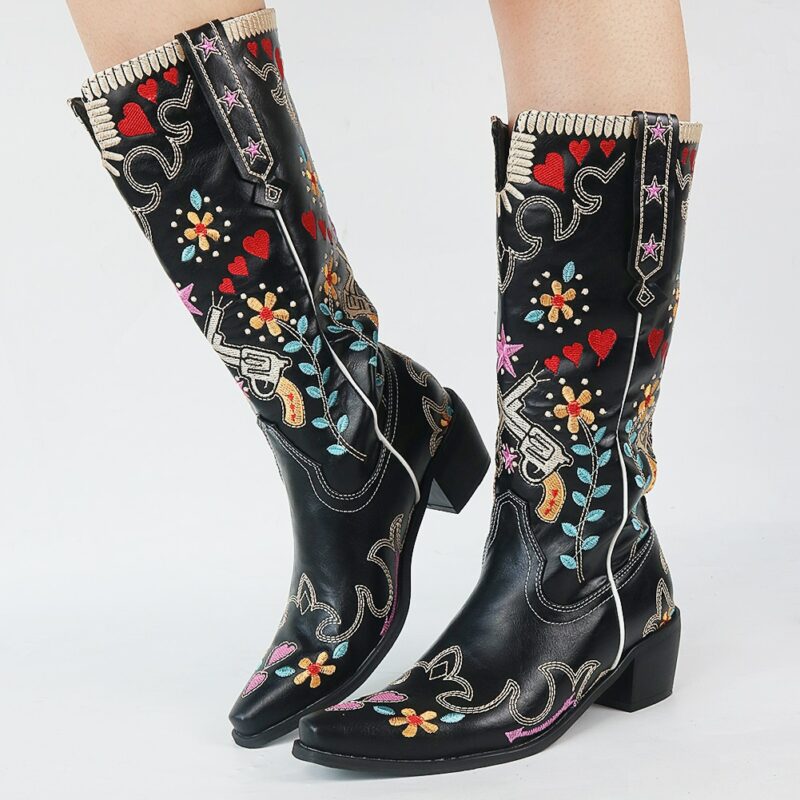 paire de bottes de cowboy noir avec des motifs colorés, portées par un e femme dont on ne voit que le bas des jambes