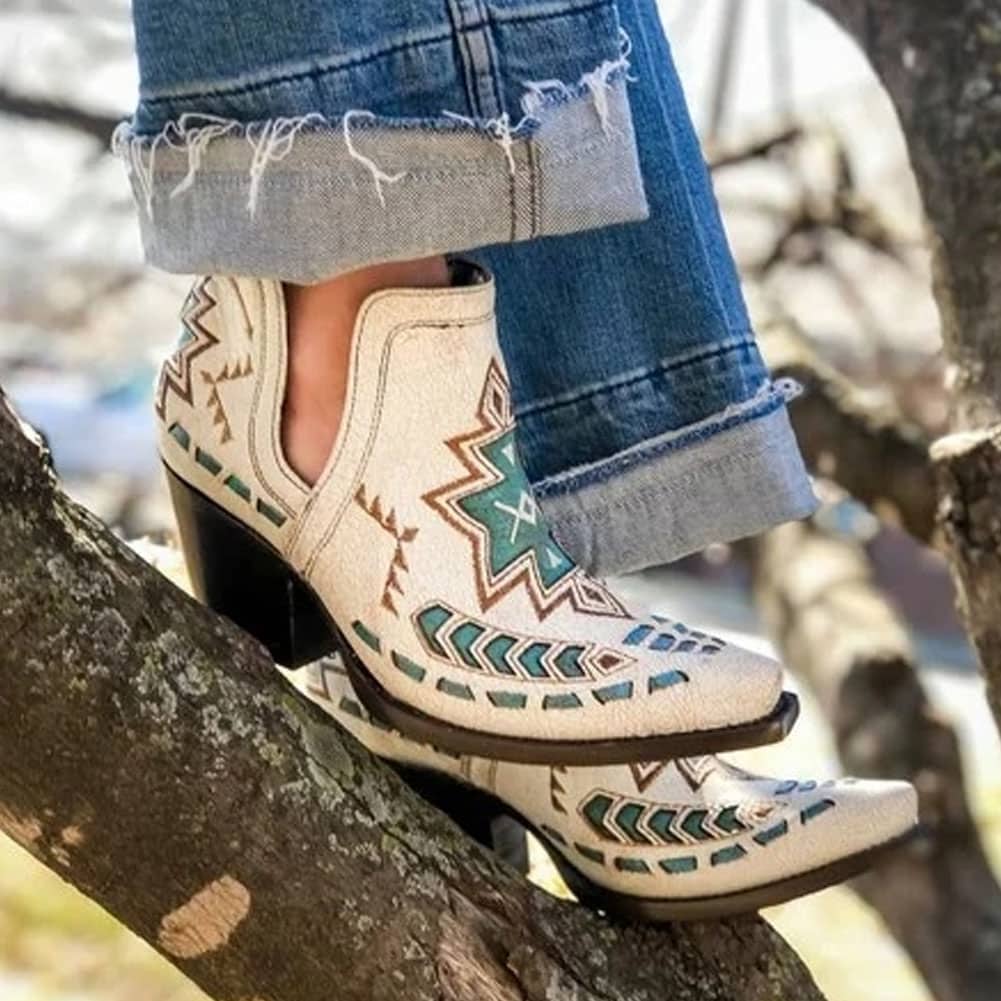 Femme qui porte un jean et une paire de bottes de cowboy basse blanche avec des motif brodés bleus, elle se trouve sur une branche et on ne voit que les pieds