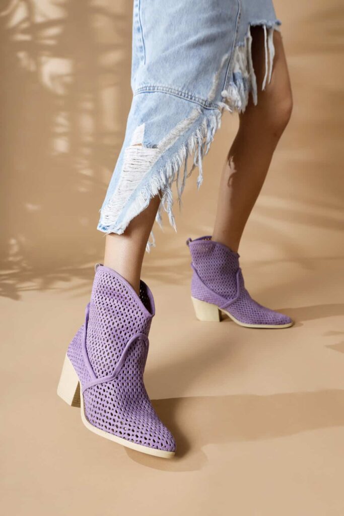 bottes d'été basses violettes avec talon bas et carré portées par une femme dont on ne voit que les jambes et qui porte une jupe longue en jean