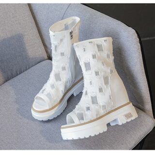 posée sur un fauteil gris , une paire de bottes blanches d'été, basses, en dentelle avec des motifs carrés, et ouvertes sur les orteils